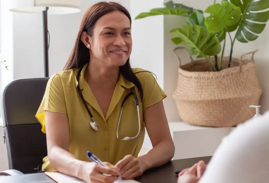 Smiling healthcare professional with a stethoscope, taking notes during a consultation