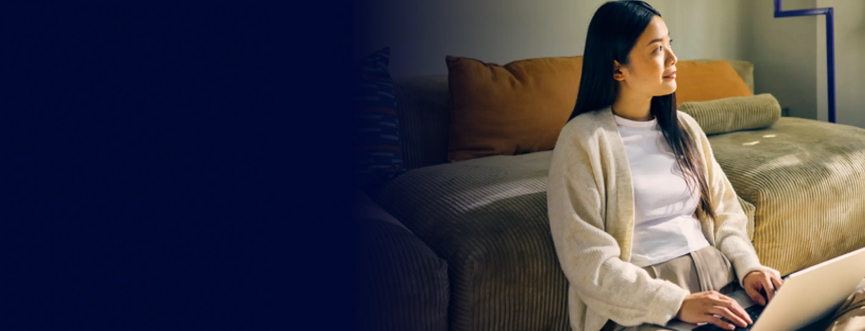 Woman sitting on a couch, looking to the side while using a laptop on her lap.