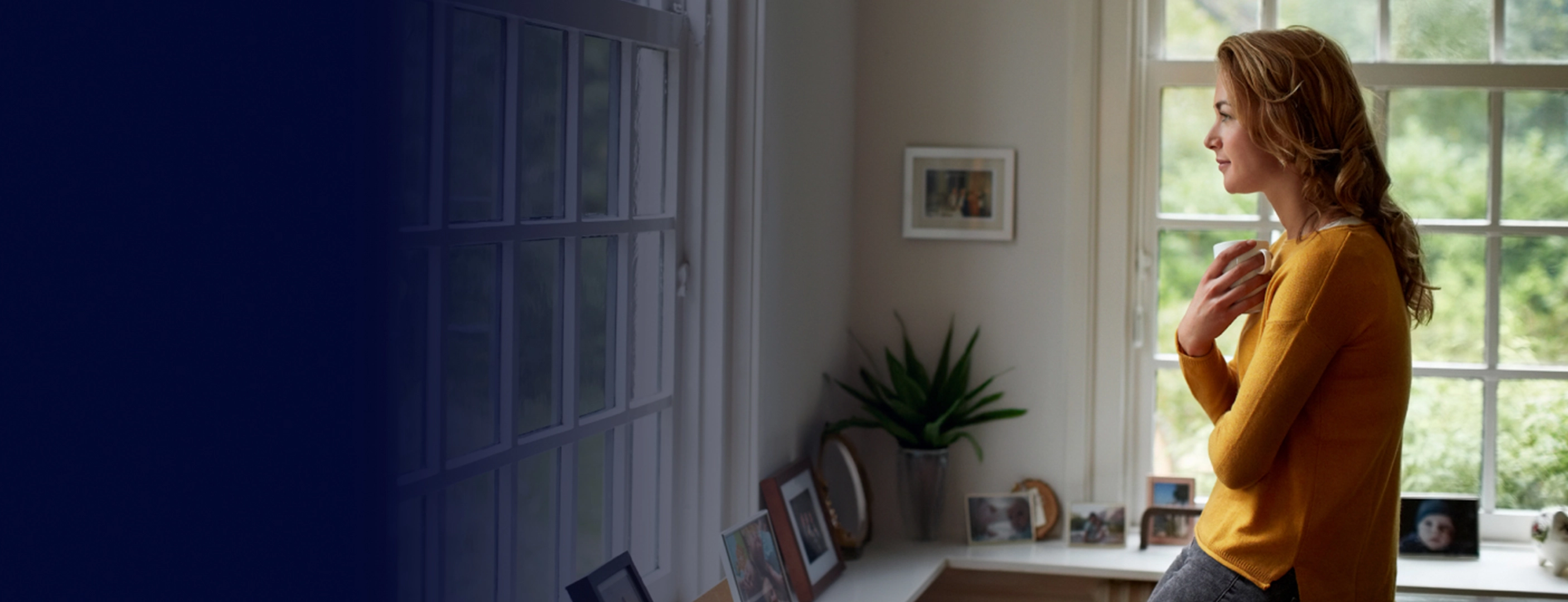 Photo of a women holding a coffee cup looking out the window