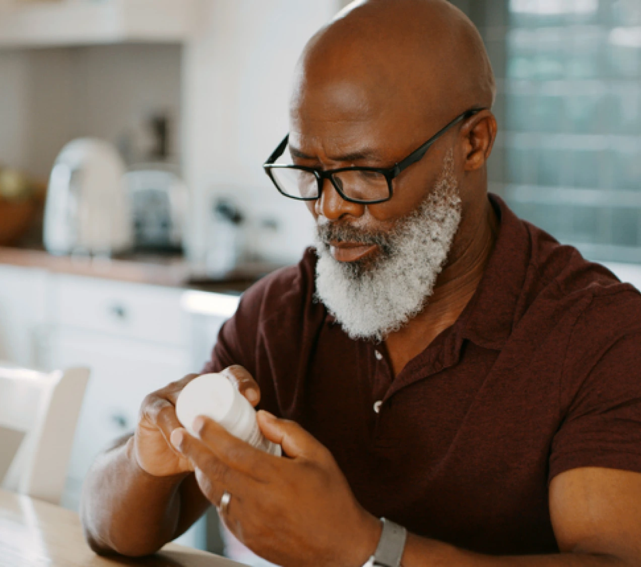 Photo of Man hin his kitchen holding a white pill bottle looking at it 